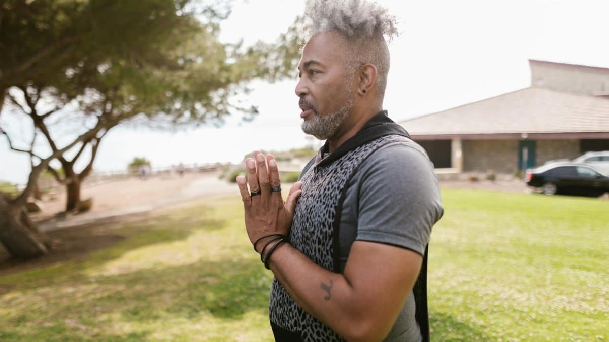 Adult man practicing meditation outdoors in a sunny park, focusing on mental wellness.