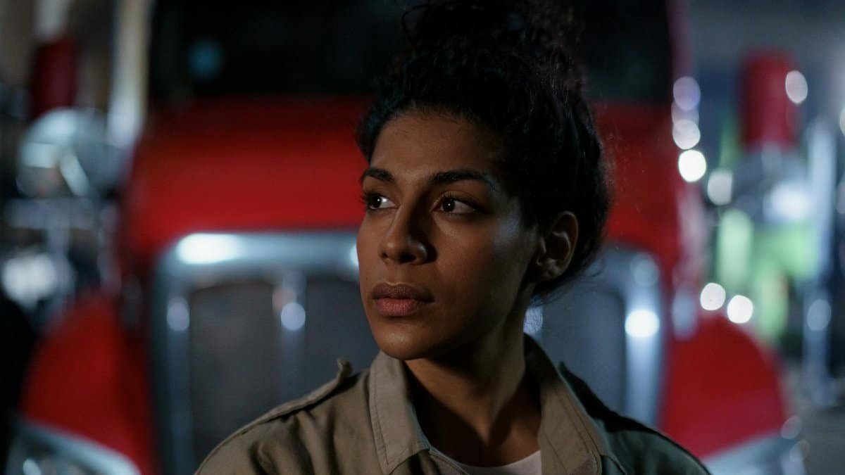 Woman in uniform looking away thoughtfully in front of a truck at night.
