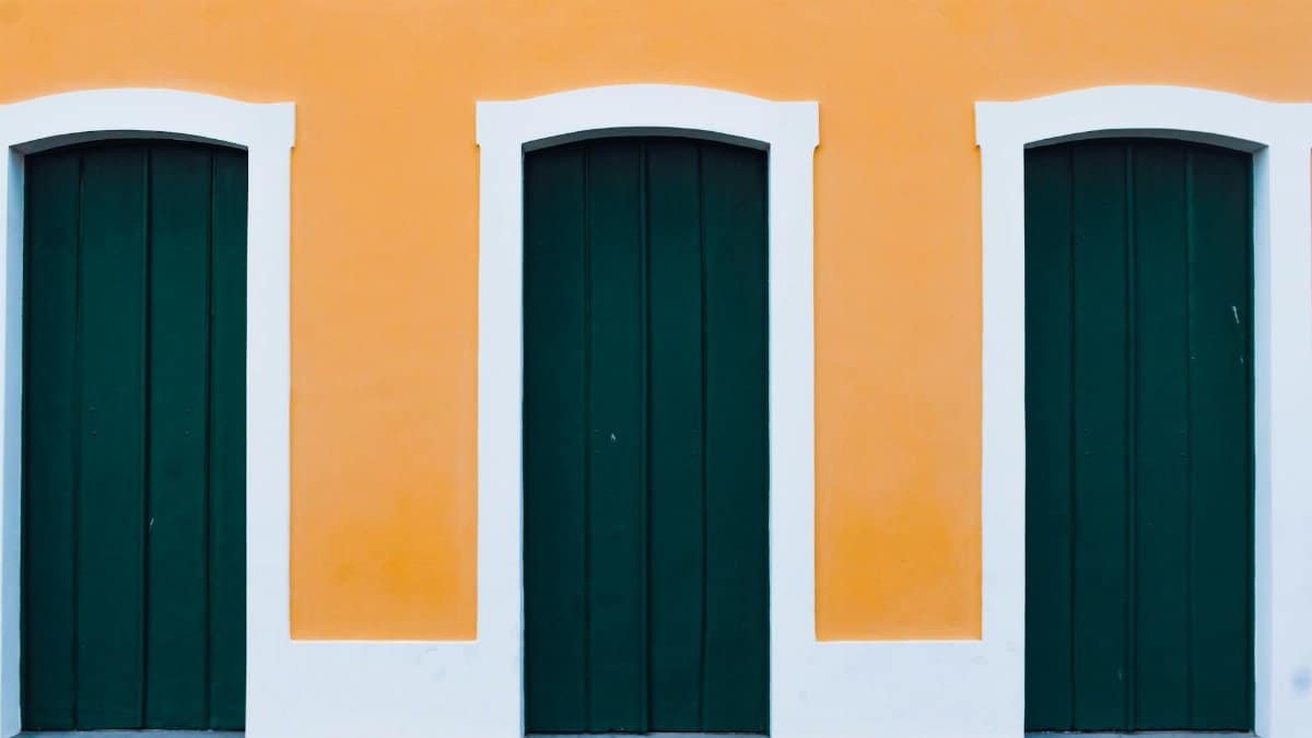 Vibrant orange facade with three green wooden doors in a symmetrical architectural design.