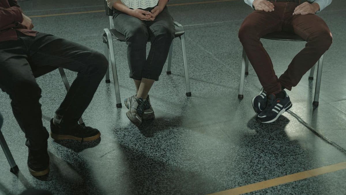 A group of three adults sitting in chairs during a discussion or support session indoors.
