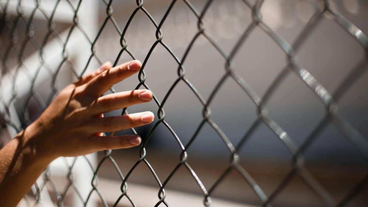 A close-up of a human hand gently touching a chain link fence, symbolizing solitude and contemplation.