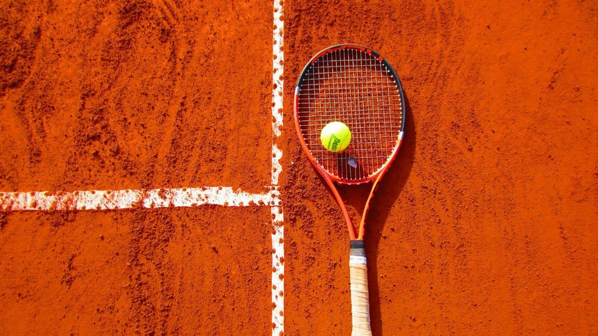 Tennis racket and ball on red clay court, ideal for sports-themed content.