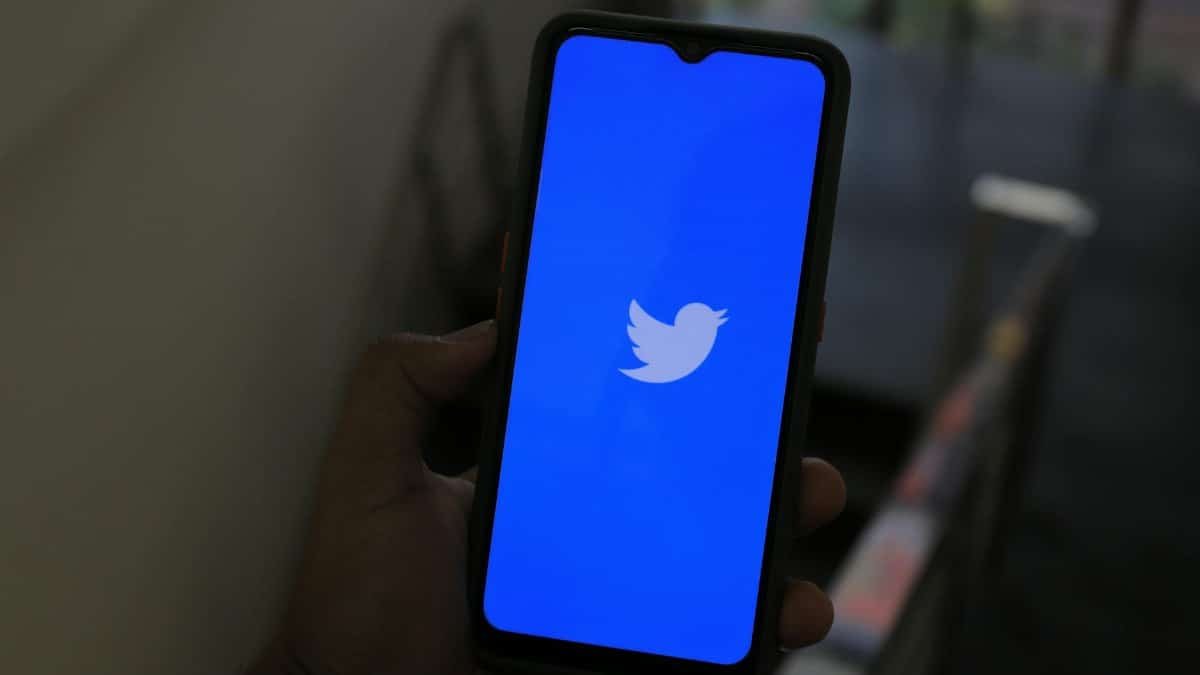 Close-up of a hand holding a smartphone displaying the Twitter app screen.