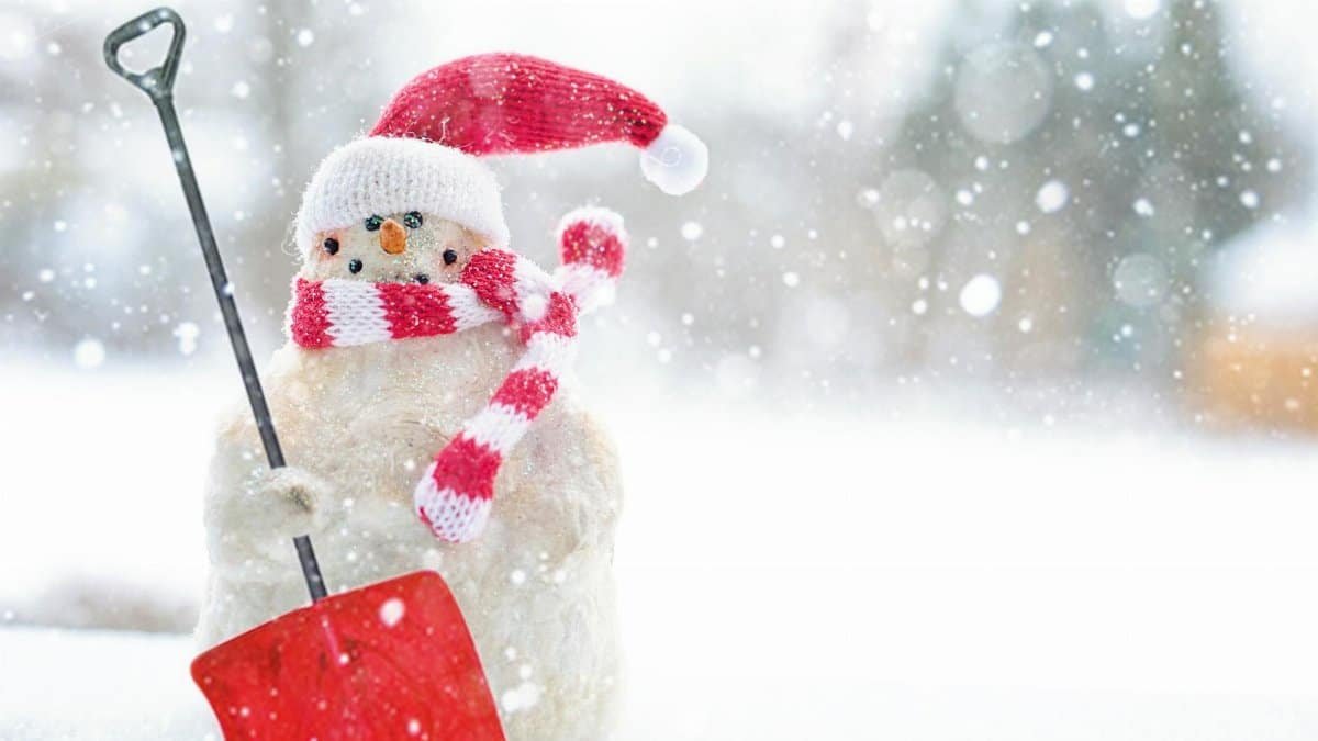 Charming snowman wearing a Santa hat and scarf with a red shovel in a snowy setting.