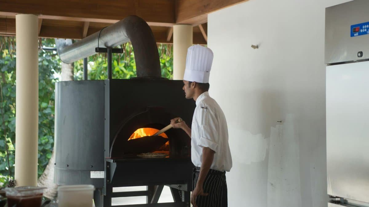 A chef prepares food using a traditional pizza oven indoors, showcasing culinary expertise.