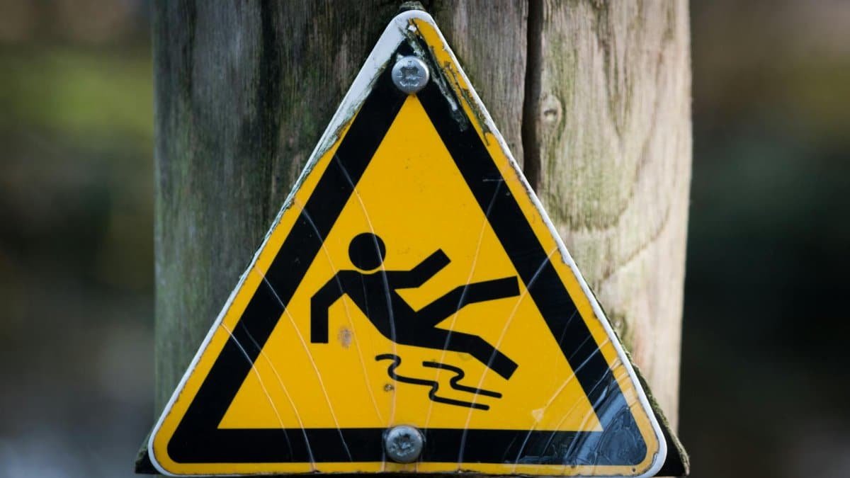 Close-up of a triangular warning sign indicating a slippery surface, fixed to a wooden post.