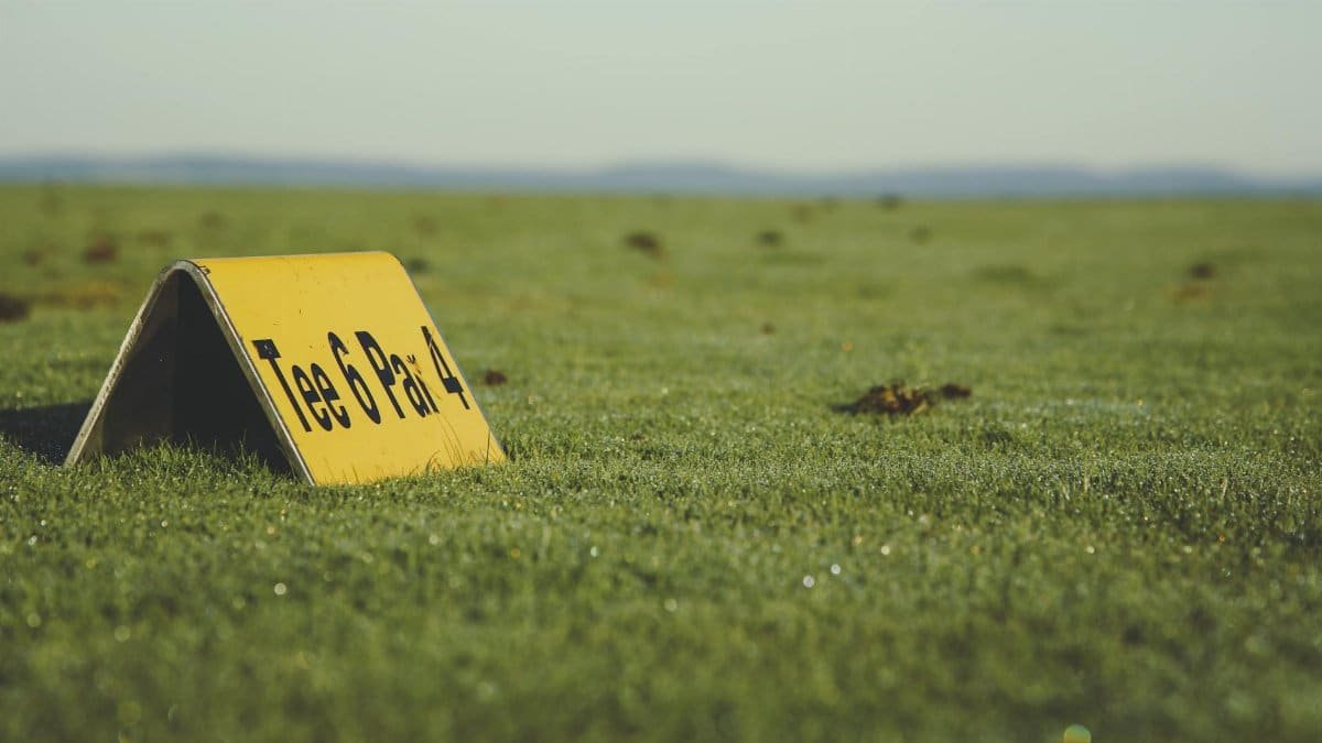 Close-up of a Tee 6 Par 4 sign on a golf course green field under clear skies.
