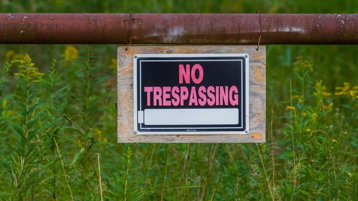 No trespassing sign on a rusty fence in a grassy field