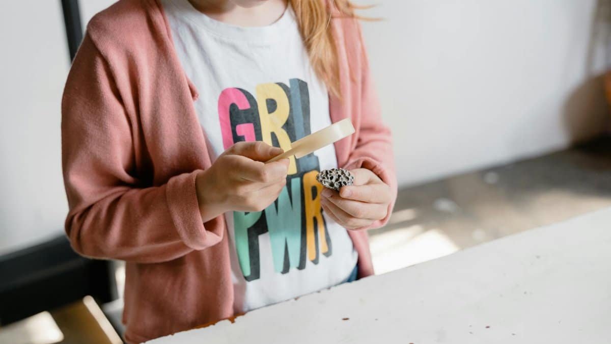 Young girl explores a rock with a magnifying glass, showcasing curiosity and learning indoors.