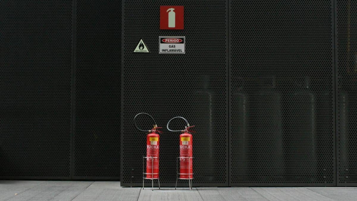 Red fire extinguishers against industrial metal wall with warning signs.