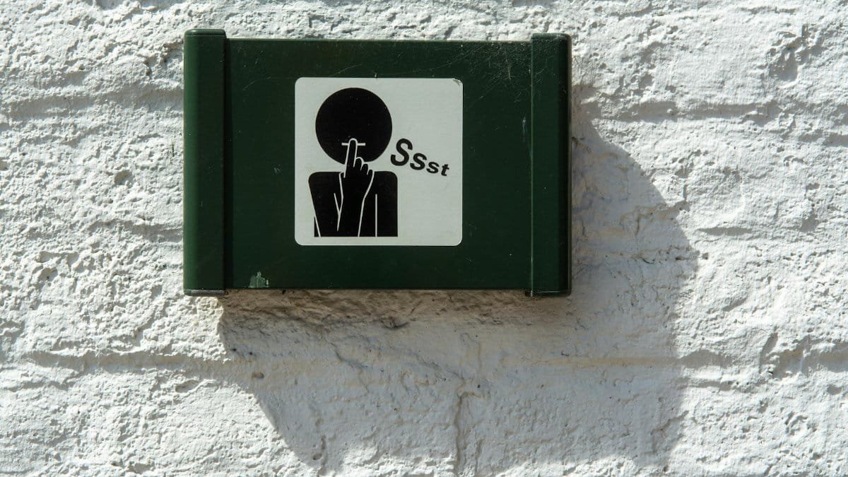A green sign on a white brick wall indicating silence with a 'Ssst' symbol.