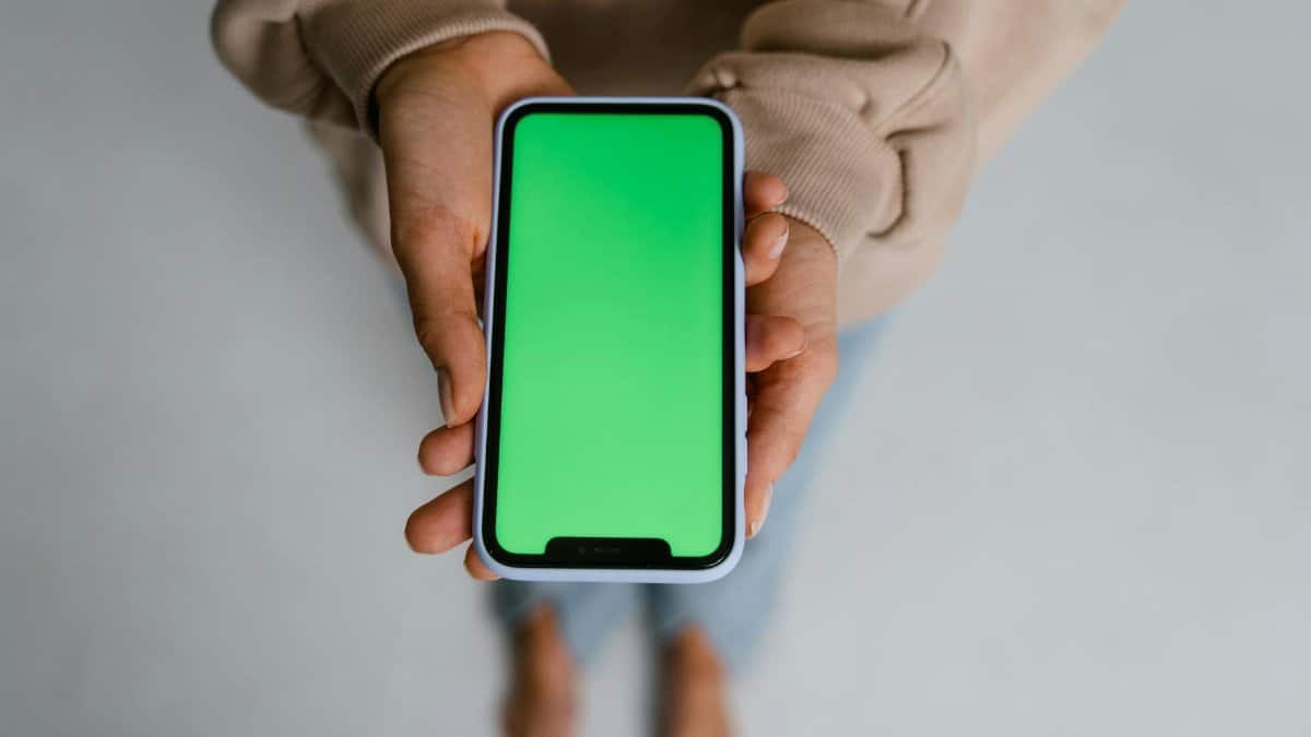 Close-up of a person holding a smartphone with a green screen background, perfect for digital content overlays.