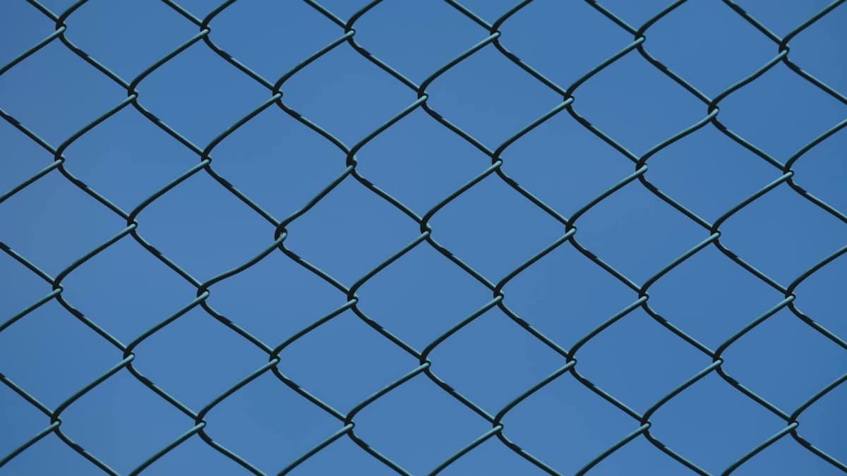 Close-up of a metal chain link fence with clear blue sky in the background, symbolizing urban security and boundaries.