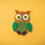 Bright felt owl craft on a vivid yellow backdrop, ideal for design projects.