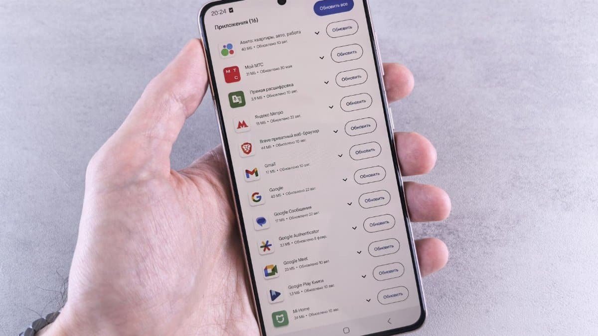 Close-up of a hand holding a smartphone displaying app updates on a light background.