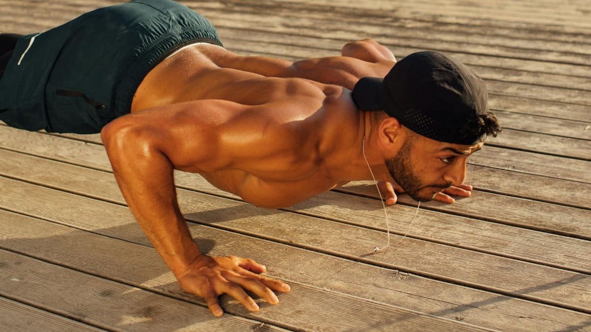 Shirtless man performing push-ups outdoors on a sunny day, showcasing strength and fitness.