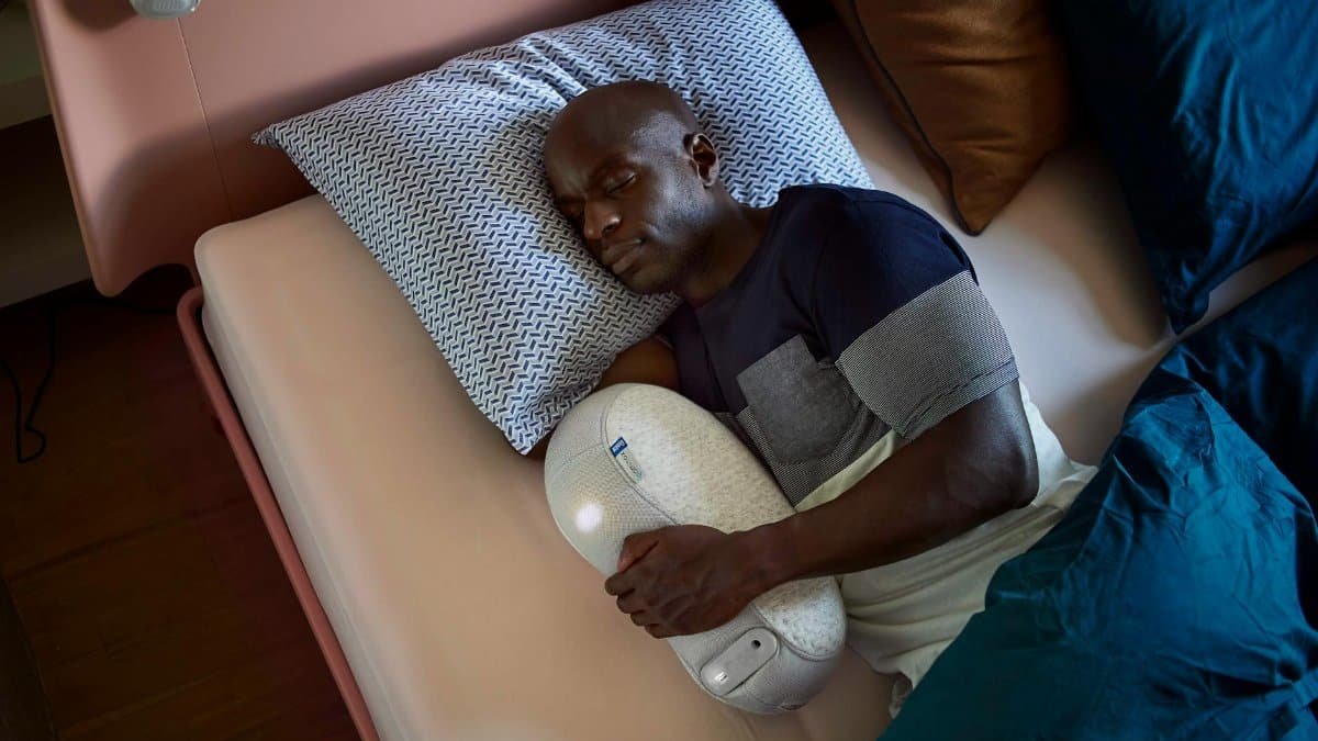 Adult man sleeping with a sleep robot for enhanced relaxation in a cozy bedroom setting.