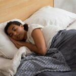 A woman peacefully sleeping in bed using a cozy weighted blanket, promoting relaxation.