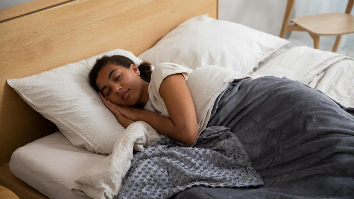 A woman peacefully sleeping in bed using a cozy weighted blanket, promoting relaxation.