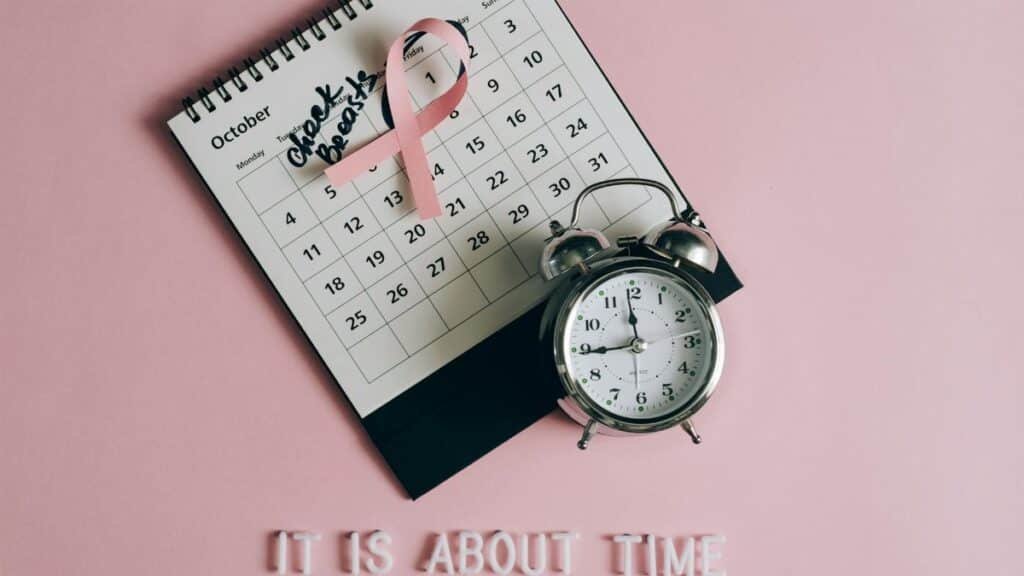 Calendar with pink ribbon, an alarm clock, and the text "Check breasts" signifies Breast Cancer Awareness.