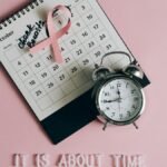 Calendar with pink ribbon, an alarm clock, and the text "Check breasts" signifies Breast Cancer Awareness.
