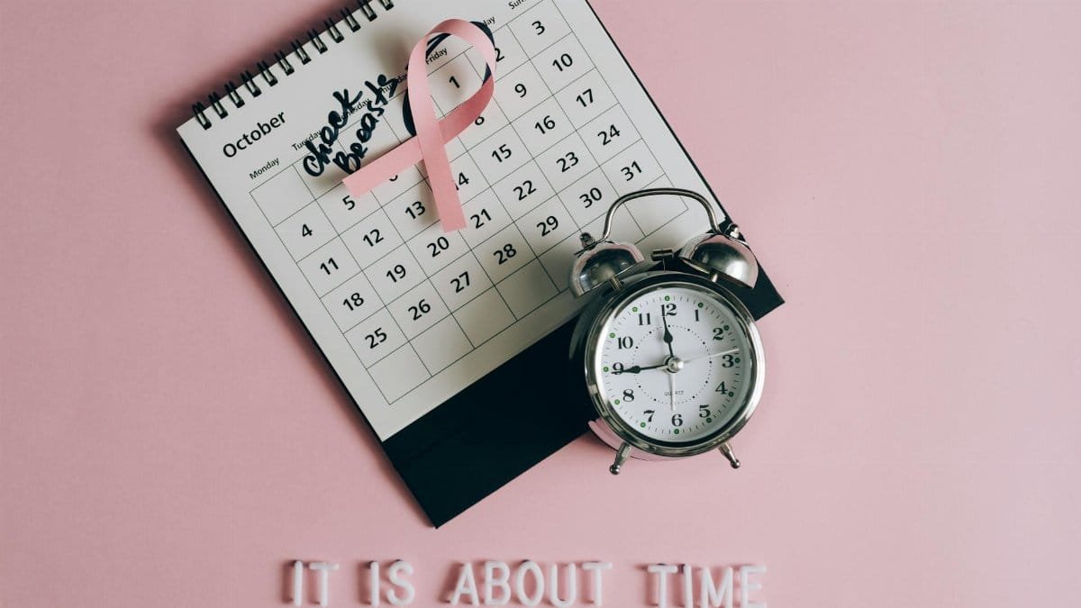 Calendar with pink ribbon, an alarm clock, and the text "Check breasts" signifies Breast Cancer Awareness.