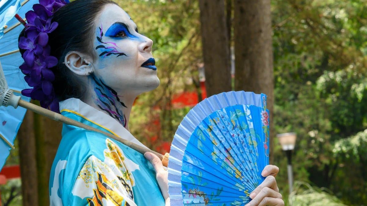 Creative portrait of a woman with artistic makeup, outdoors with fan and umbrella.