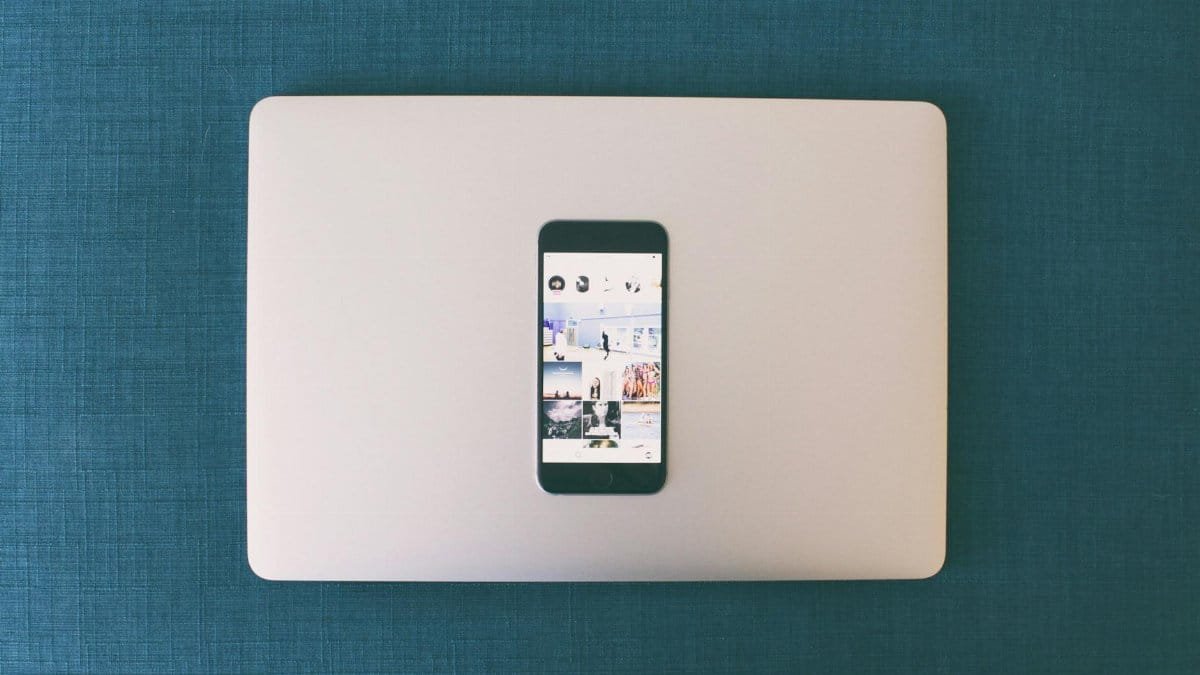 Flat lay of a smartphone on a laptop with social media photos on screen.