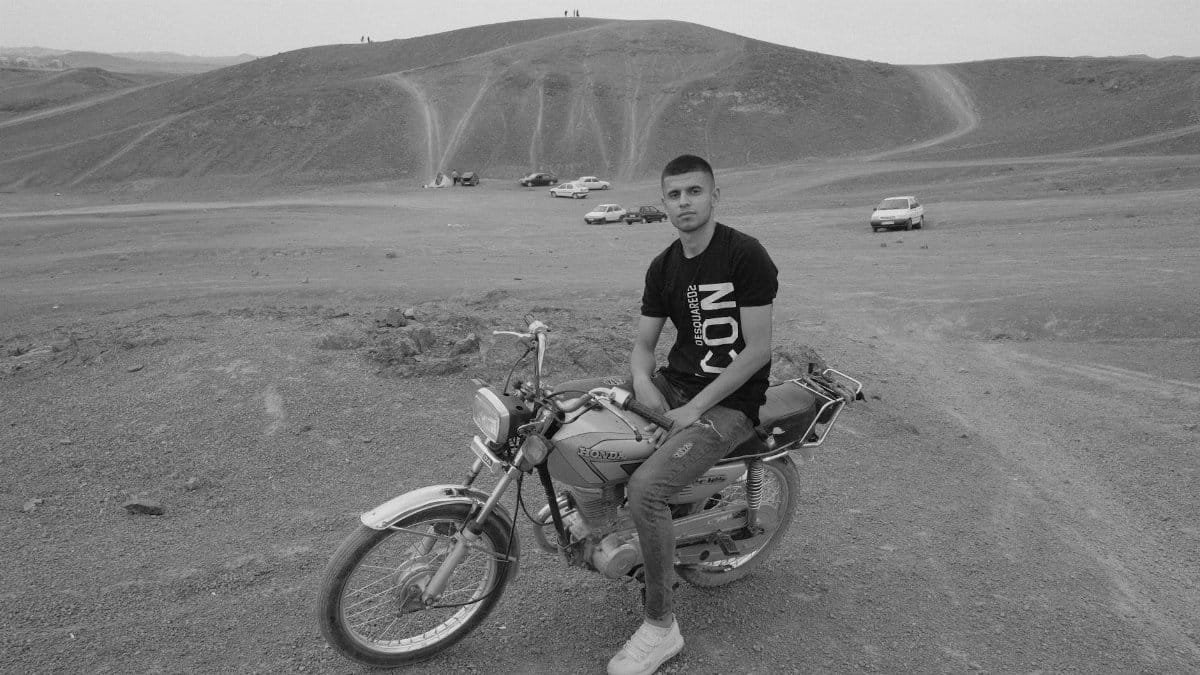 A young man sitting on a motorcycle in a rural desert area. Black and white photo.