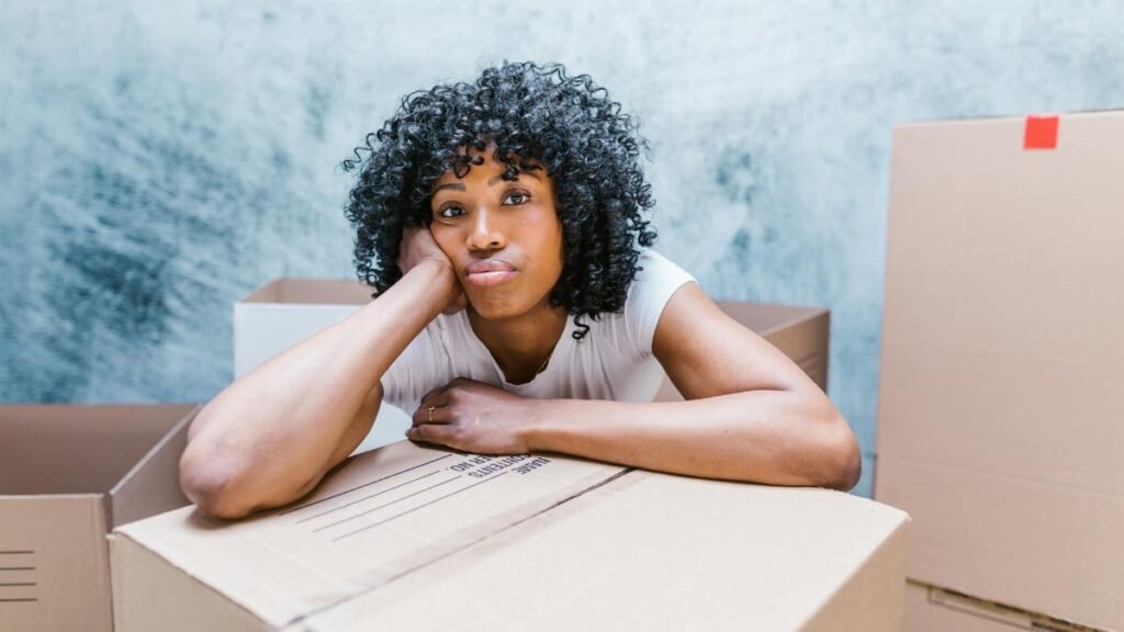 Tired woman leaning on a moving box while packing and relocating to a new home.