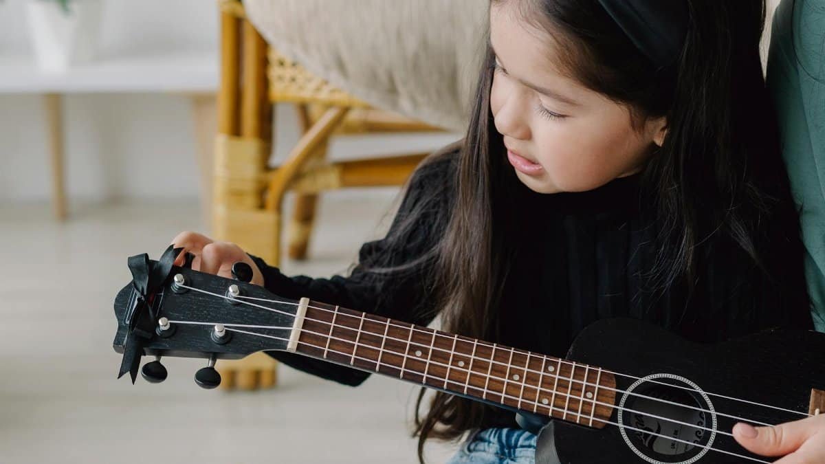 A young girl learns to play the ukulele, focusing on tuning the instrument, creating a peaceful home learning moment.
