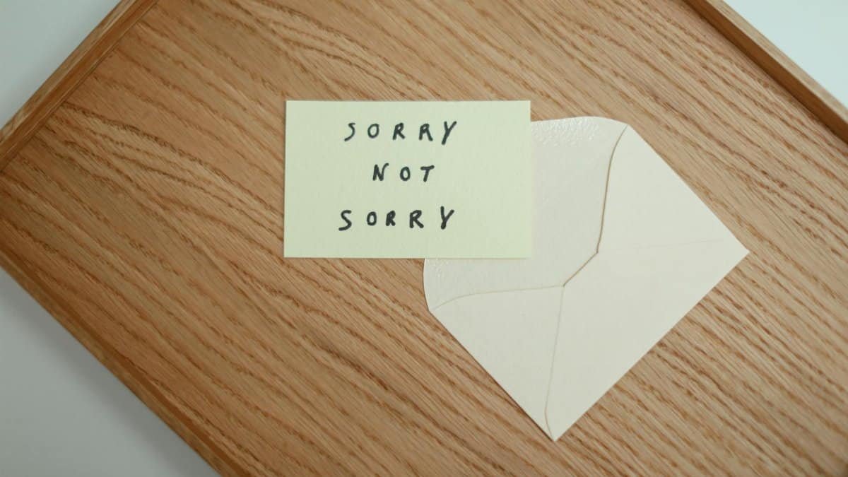A flat lay of a 'Sorry Not Sorry' card with an envelope on a wooden surface.