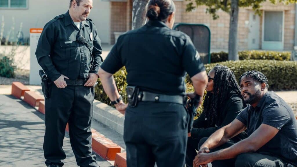 Police officers interacting with seated individuals in an urban outdoor setting.