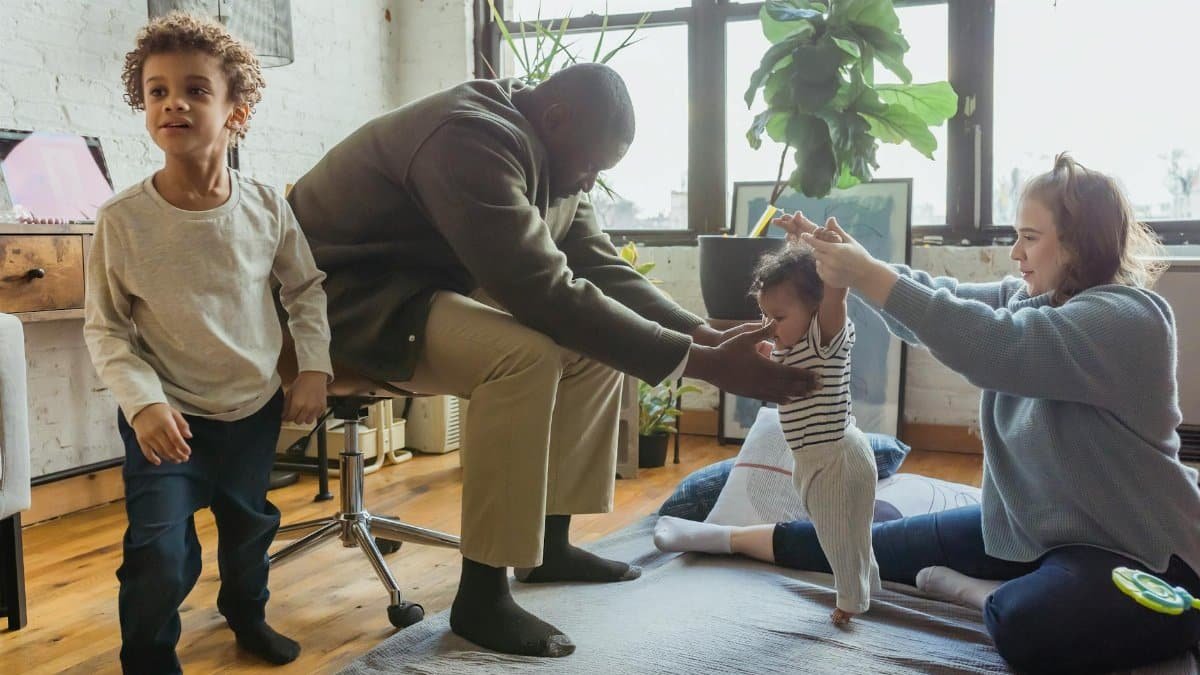 Multiracial family playing with children in casual outfit on textile on floor in light room near windows