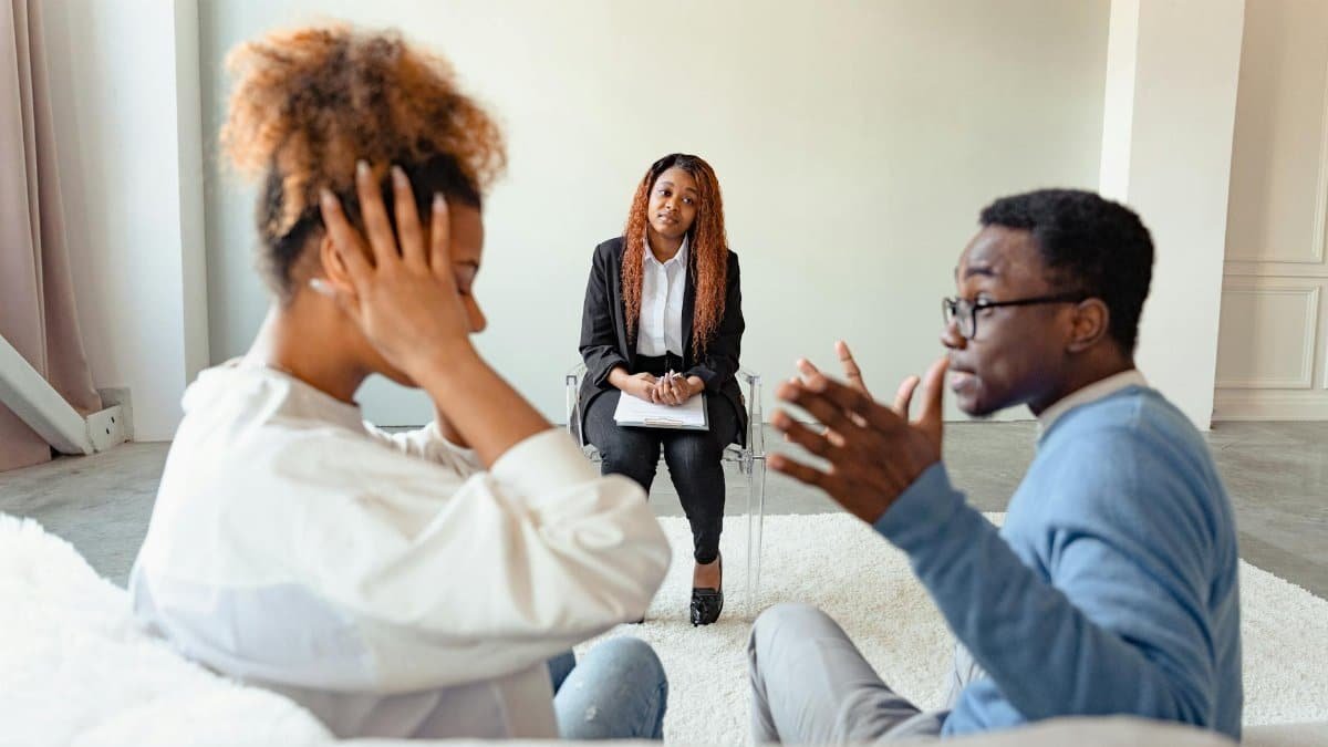 A couple in therapy session with a mental health professional indoors.