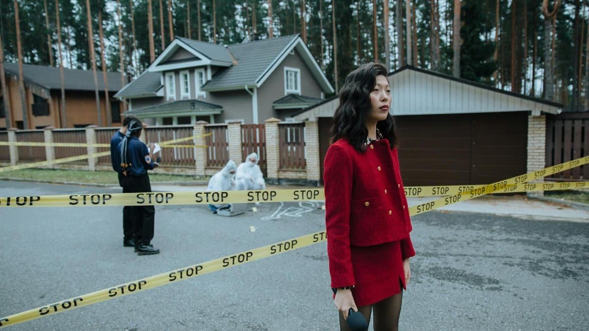 A woman reporter in a red outfit at a crime scene marked with caution tape, outdoors near houses.
