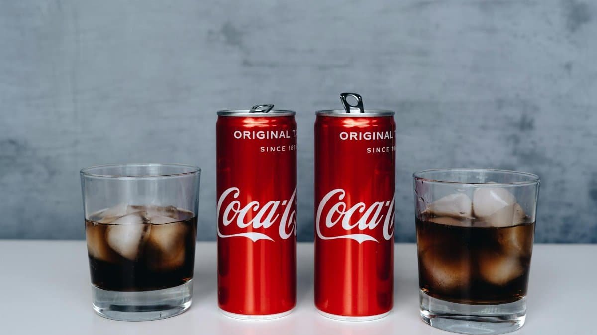 Two cans of soda with ice-filled glasses on a minimalistic background.