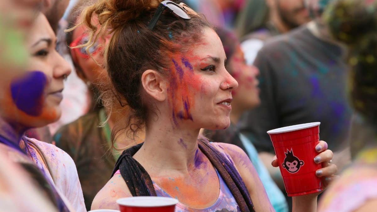 People enjoying a vibrant celebration with colorful face paints and drinks in New York.