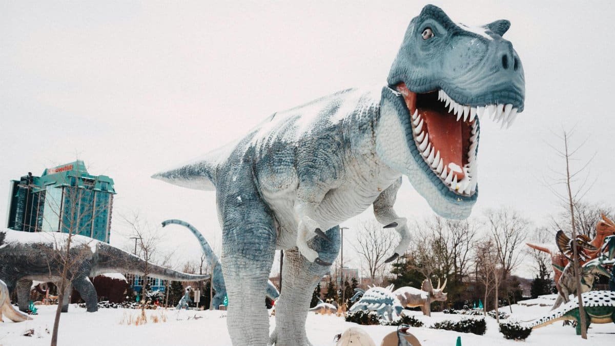 Winter scene of realistic dinosaur statues in a snowy outdoor park setting, featuring a roaring T-Rex.