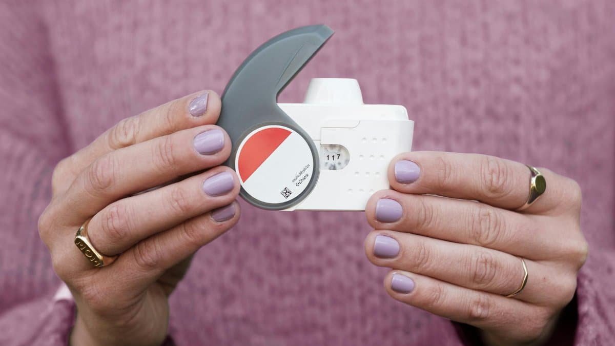 Hands with purple nail polish holding a modern eye drop dispenser.