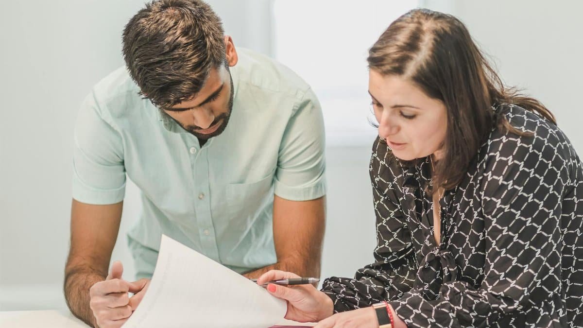 Real estate agent assisting first-time homebuyer with documents inside a bright room.