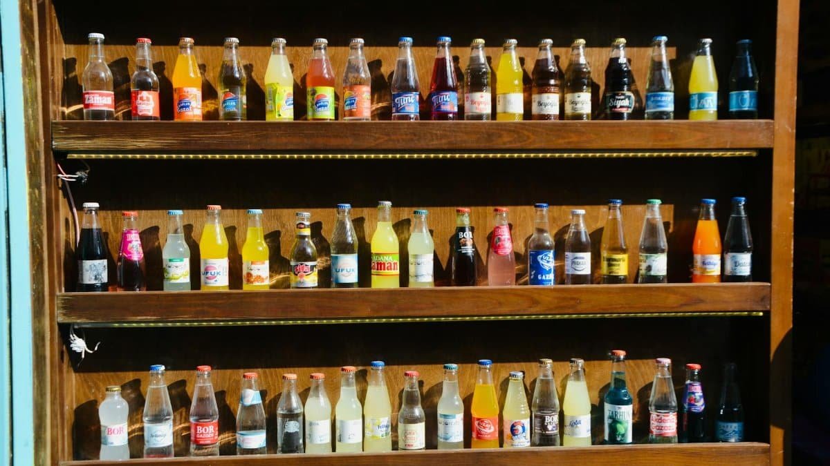 Colorful assortment of soda bottles displayed on wooden shelves in a store setting.