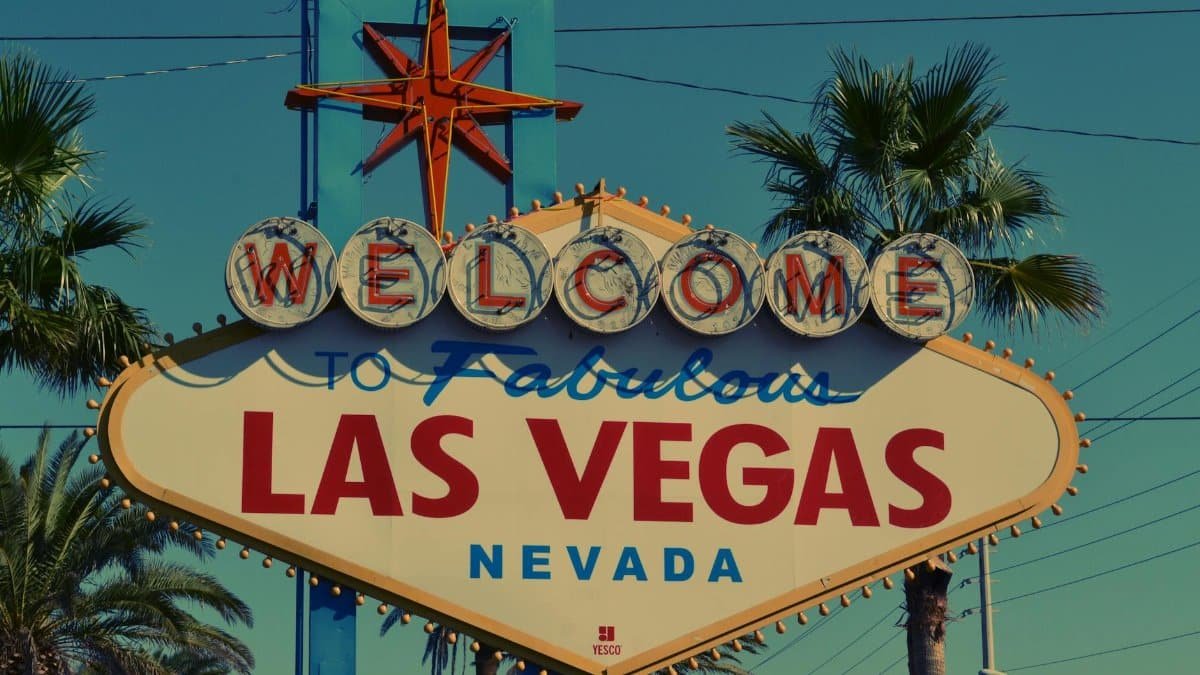 The famous Welcome to Las Vegas sign framed by palm trees under clear skies.