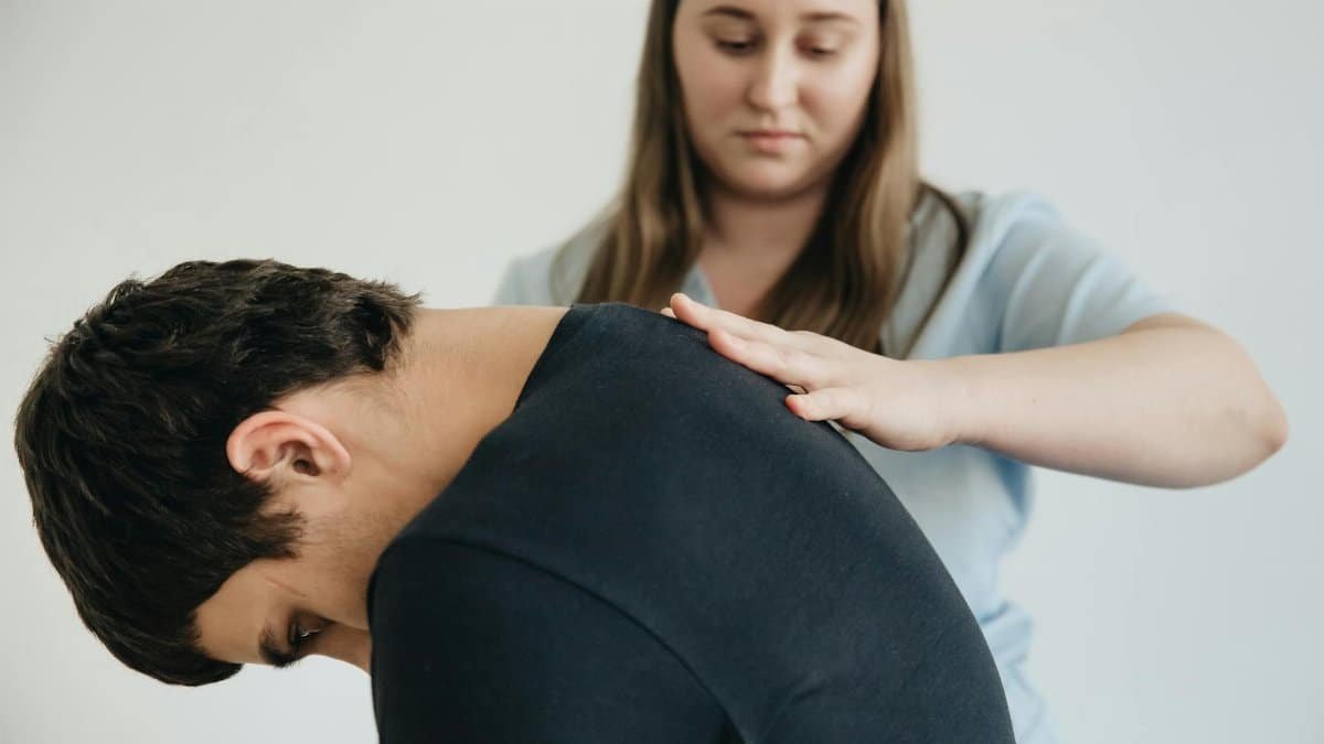 A physiotherapist assisting a patient with back pain in an indoor clinic setting.