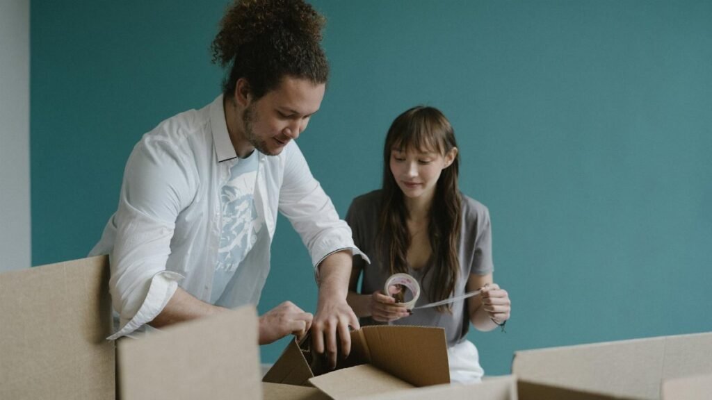 Young couple smiling while unpacking boxes in their new apartment. Moving in and home concept.