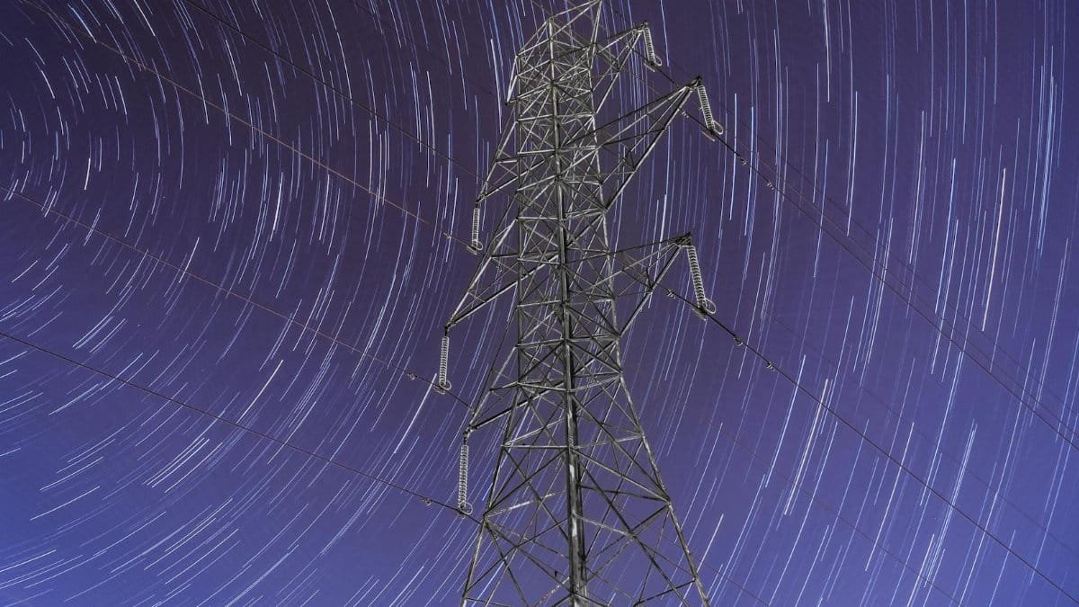 Nighttime long-exposure captures star trails over a towering power pylon in Quebec City, Canada.