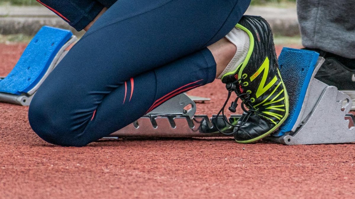 Close-up of a runner's legs ready to start a race, showcasing running shoes and starting block.