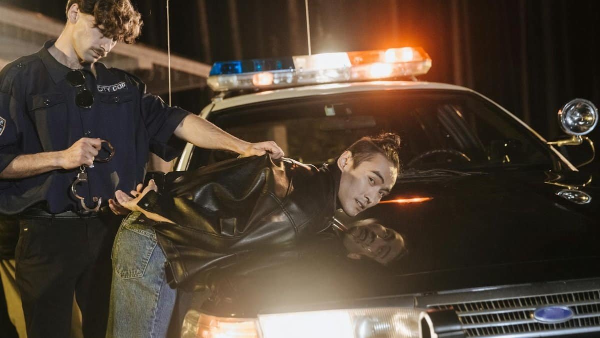 A police officer handcuffing a suspect on a patrol car at night.
