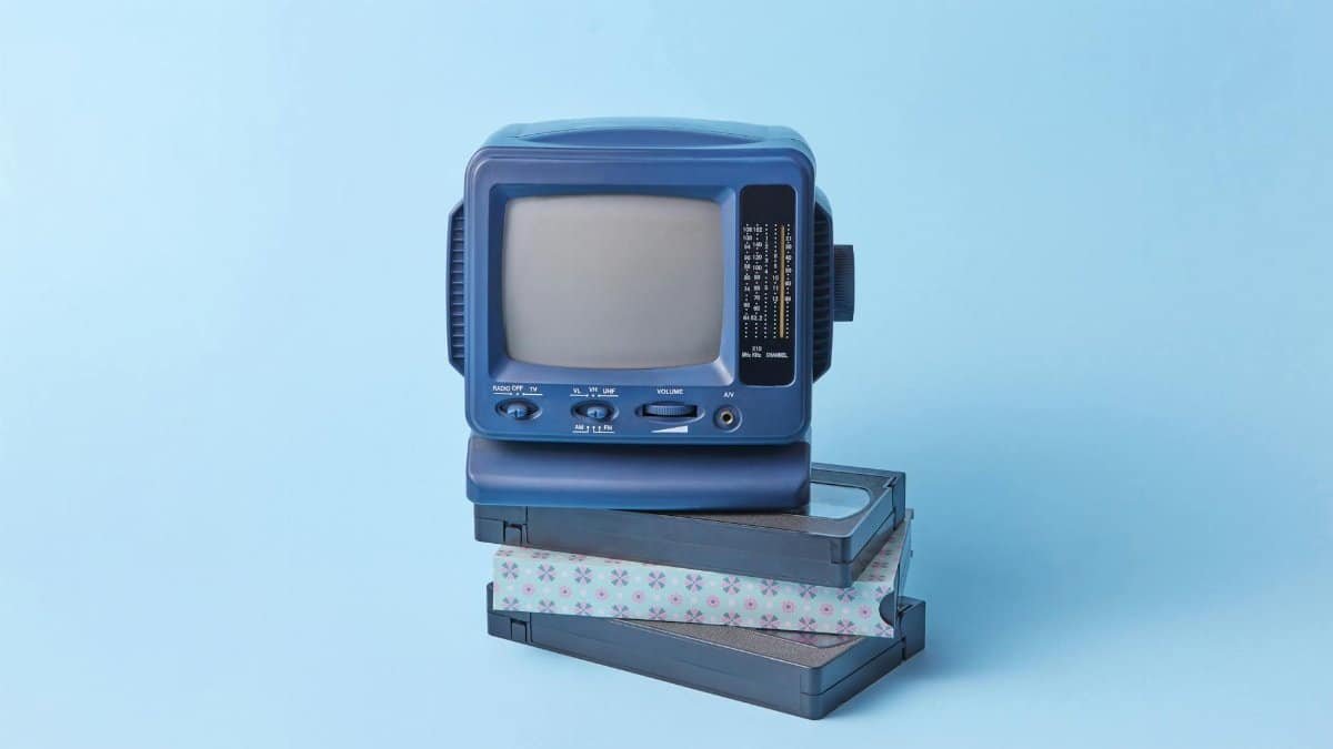 Vintage blue TV set featured atop VHS tapes on a pastel blue background, evoking a retro vibe.