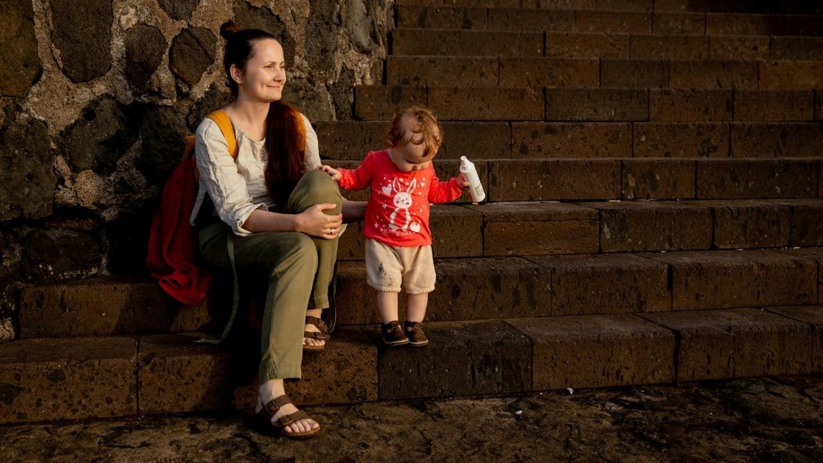 A mother and toddler enjoying a sunny day on stone steps outdoors, sharing a bonding moment.